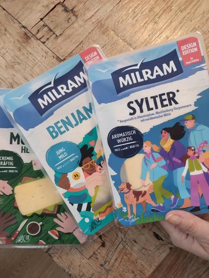 Drei Packungen Milram-Käse in der Design-Edition, die mit Illustrationen verschiedener Künstler*innen gestaltet sind und jeweils Menschen verschiedener Haut- und Haarfarbe zeigen.